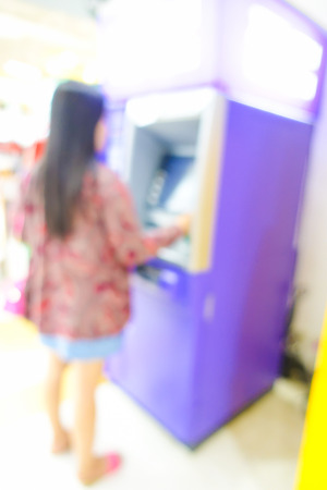 Blurred image of woman use ATM machine in bank to take money or do something about financial.の写真素材