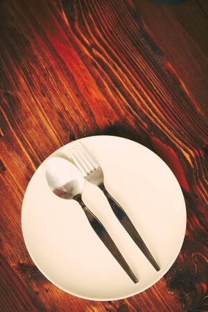 Metal spoon and fork on white plate put on wooden table.の写真素材
