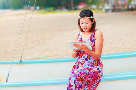 Smiling women using tablet computer with colorful dress sitting at the beachの写真素材
