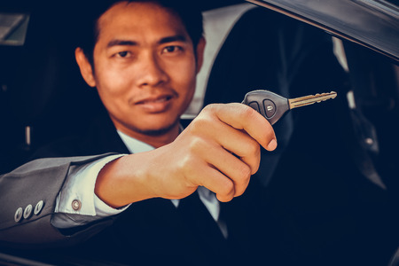 Business man smiling showing key and sit in carの写真素材