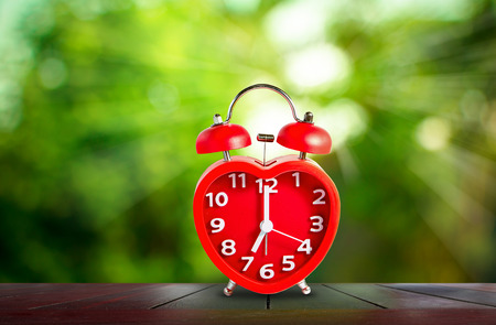 Red clock mark on 7 o'clock put on wooden tabletop with abstract blurred on fresh green nature...