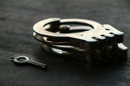 Handcuffs with key put on wooden tableの写真素材