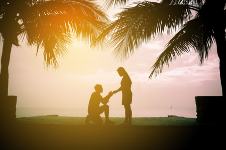 Young adult male groom and female bride holding hands on beach at sunsetの写真素材
