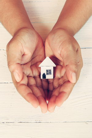 Hands holding little wooden house  model on table backgroundの写真素材