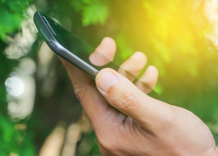 Close up human hand use mobile phone with fresh green nature backgroundの写真素材