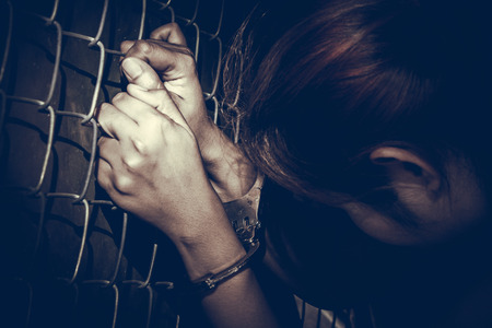 Sad woman with handcuffs holding rust metal fence with dark tone styleの写真素材