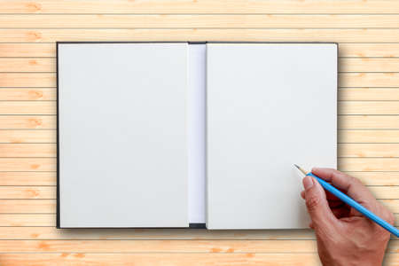 Human hand use blue pencil to write open notebook put on brown wooden tabletop with white space for...