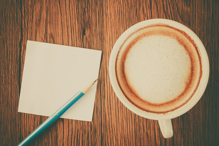 Cup of cappuccino coffee with pencil and blank white paper put on brown wooden table topの写真素材