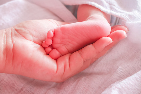 Close up mother hands holding infant feet sleeping in the bedの写真素材