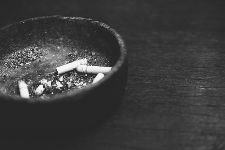 Cigarette butts with ash in ashtray on wooden tableの写真素材