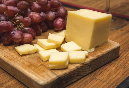 Ripe red grapes and white cheese on a wood block.の写真素材