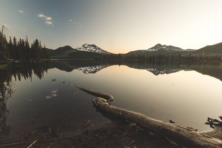 Beautiful sunrise view of Sparks Lake near Bend, Oregon. Large tree root in foreground with two mountain peaks in distance. Morning, summer or spring setting.の写真素材