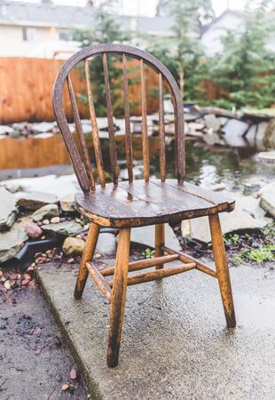 Antique, wooden chair in a home back yard near a pond in wet winter weather.