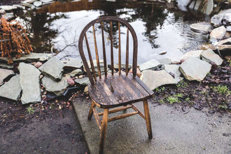 Antique, wooden chair in a home back yard near a pond in wet winter weather.の写真素材