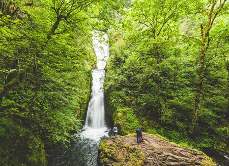 People standing on a rock platform in front of a waterfall in the Columbia River Gorge. Oregon, USA.の写真素材