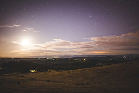 Night sky with bright moon over rolling hills.の写真素材