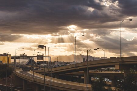 Sunlight beaming through dark clouds over the desert in Las Vegas, Nevada. Freeway overpass, city buildings, and distant mountains on a beautiful stormy day.の写真素材