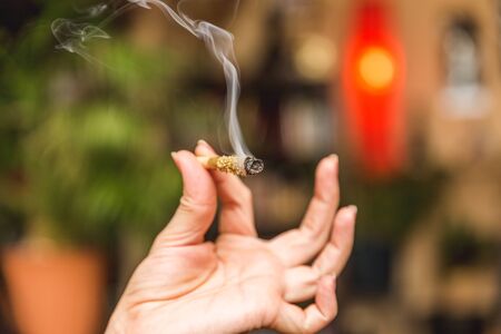 Smoke streams from the end of a burning joint in a woman's hand. Joint is covered in oil and kief or THC powder.の写真素材