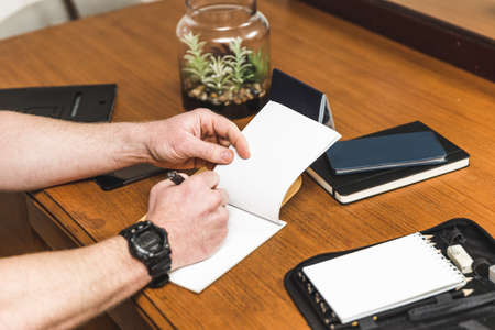 Man writing in a notepad on a desk in an office.の写真素材