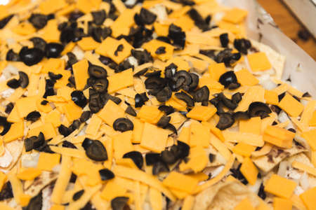 Cheddar cheese and black olives on top of chips. Ingredients for nachos.の写真素材