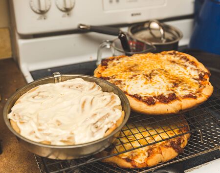 Baked goods cooling on metal racks. Cinnamon rolls and two pizzas cooling in a home kitchen.の写真素材