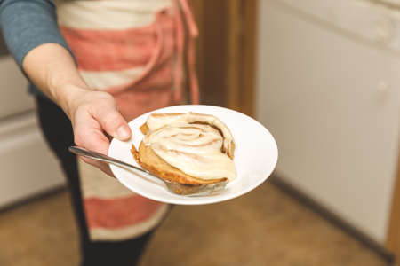 Woman in apron holding plate with homemade cinnamon roll and fork.の写真素材