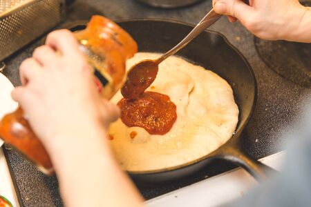 Chef pours tomato sauce onto pizza crust in a cast iron pan while making pizza.の写真素材