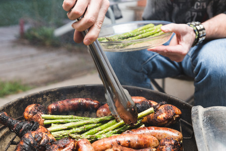 Man moving asparagus in between grilled meat while barbecuing outside.の写真素材