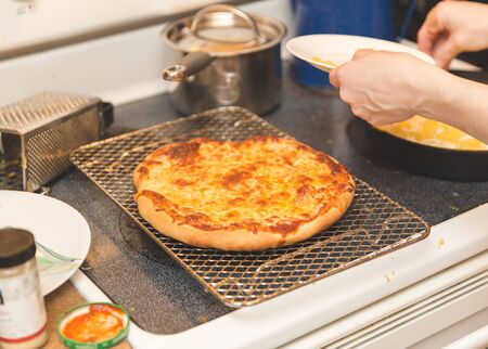 Freshly-baked cheese pizza cooling down on a metal rack. Homemade cheese pizza with crispy crust.の写真素材