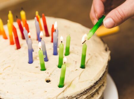 Person lighting colorful wax candles on a birthday cake.の写真素材