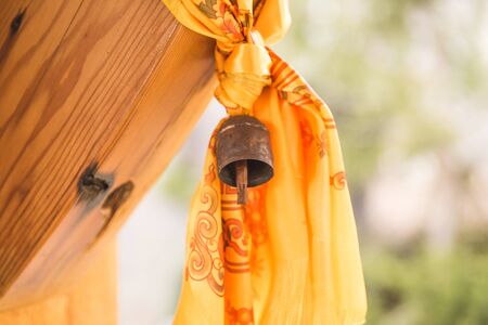 Bell with yellow and orange curtain or tapestry hanging from wooden structure.