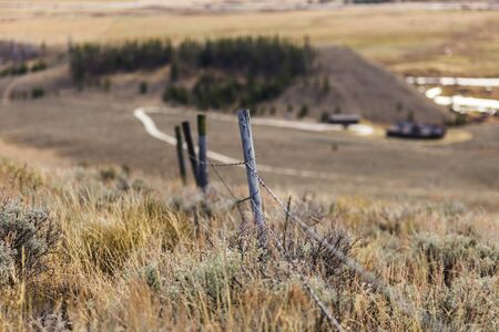 Barbed Wire Fence in high desert area with sagebrush and countryside buildings nearby.の写真素材