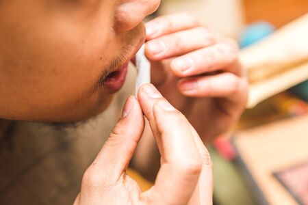 Man holds a joint near his mouth to lick the paper glue as a final step in rolling a cannabis or marijuana joint.の写真素材