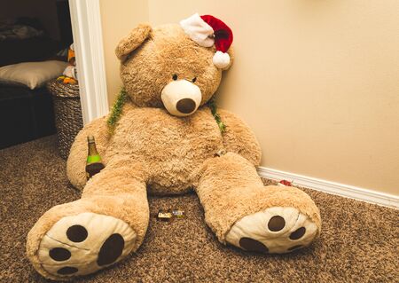 Large light brown stuffed bear wearing a santa hat sitting on carpet.の写真素材