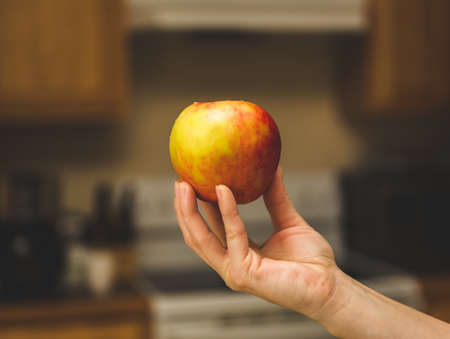 Hand holding an uneaten apple by the finger tips.の写真素材