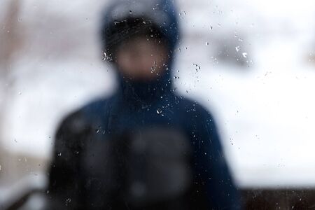 Drops of rain on a glass window with a boy in a jacket in the background.の写真素材