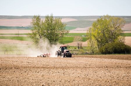 Tractor kicking up dust while working in a field in rural America.