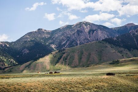 Steep mountains with light vegetation under bright and lightly cloudy blue sky. Rural high desert landscape in foreground.の写真素材