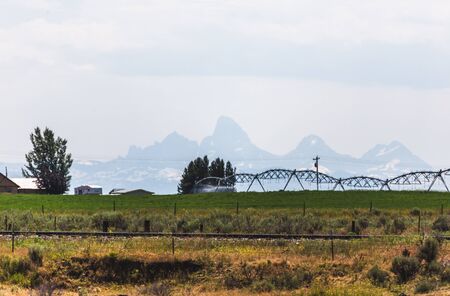 Sprinklers spray green fields with Teton Mountains in background.の写真素材