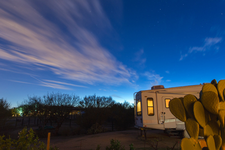 Clouds floating in a dark blue sky over a camper trailer parked in a desert landscape location.の写真素材
