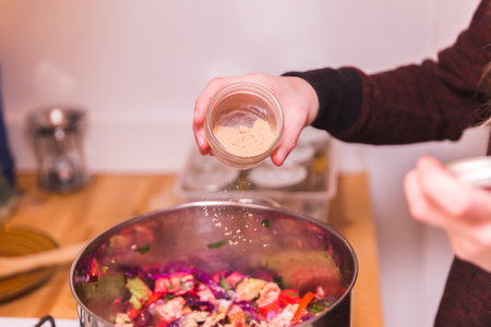 Woman sprinkling yeast onto cooking vegetables in a home kitchen.の写真素材