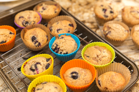 Homemade blueberry muffins baked in colorful silicone cups, cooling on a baking rack in a kitchen.の写真素材
