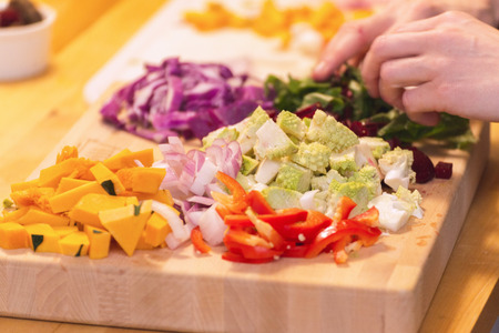Piles of chopped vegetables on a wooden cutting board or chopping block. Vegetables include squash, onions, peppers, and romanesco broccoli.の写真素材