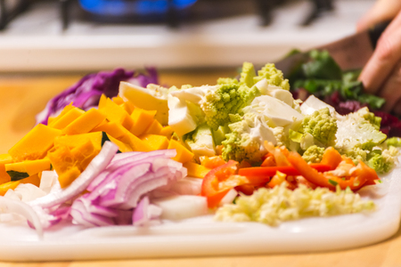 Piles of chopped vegetables on a wooden cutting board or chopping block. Vegetables include squash, onions, peppers, and romanesco broccoli.の写真素材