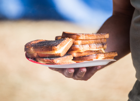 Stacks of grilled cheese sandwiches on a paper plate. Overweight man holding plate. Sandwiches are burnt and contain processed cheese and white bread.の写真素材