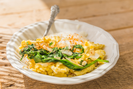 White ceramic bowl with scrambled eggs, cooked spinach, onions, and spices.の写真素材
