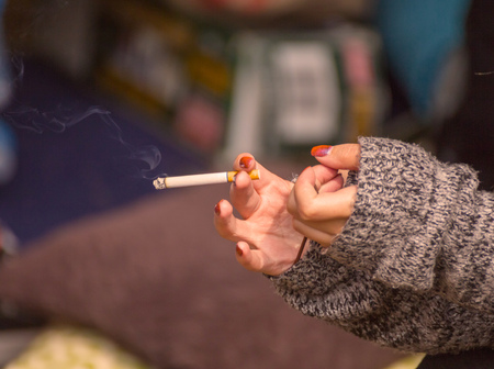 Hands of a woman in a sweater holding a burning tobacco cigarette. Indoor home setting.