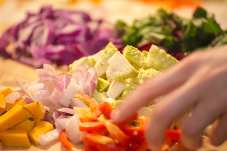 Piles of chopped vegetables on a wooden cutting board or chopping block. Vegetables include squash, onions, peppers, and romanesco broccoli.の写真素材