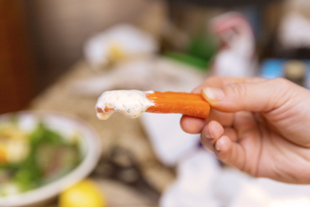 Hand holding sliced carrot dipped in ranch dressing.の写真素材