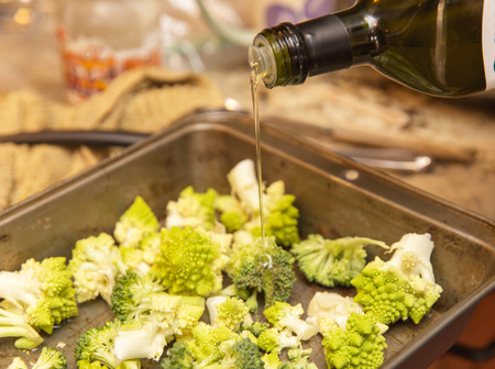 Olive oil being poured onto fresh Romanesco broccoli in a metal pan. Kitchen setting.の写真素材